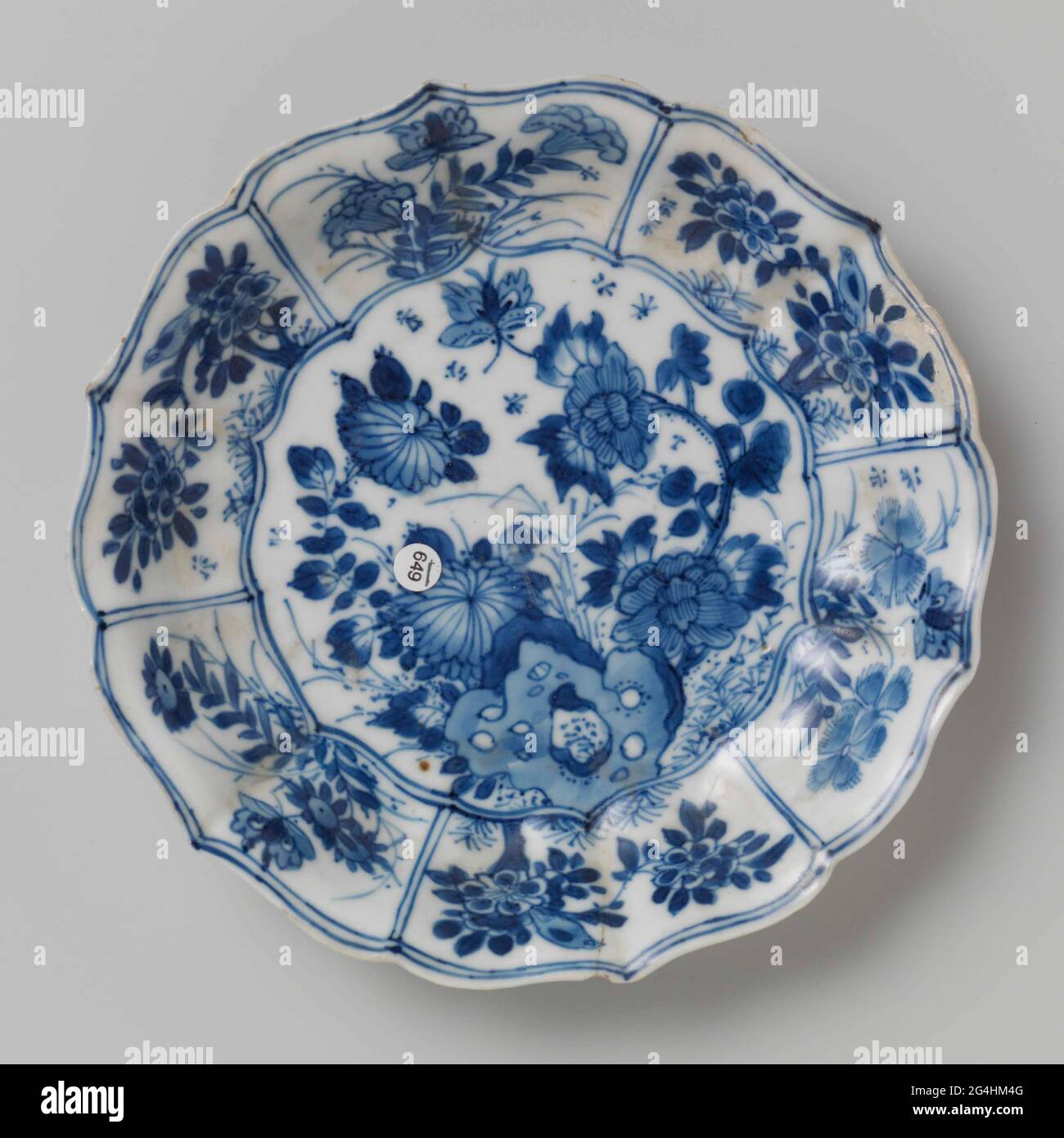 . Dish of porcelain with ribbed wall and scalloped edge, painted in underglaze blue. On the flat a rock with two flower branches (peony, chrysanthemum), a butterfly and insects; the wall divided into six compartments filled with flower branches, butterflies and birds; Three flower branches on the back. Marked on the underside with the character 'Fú' in a double circle. Three cracks in the wall. Blue White. Stock Photo