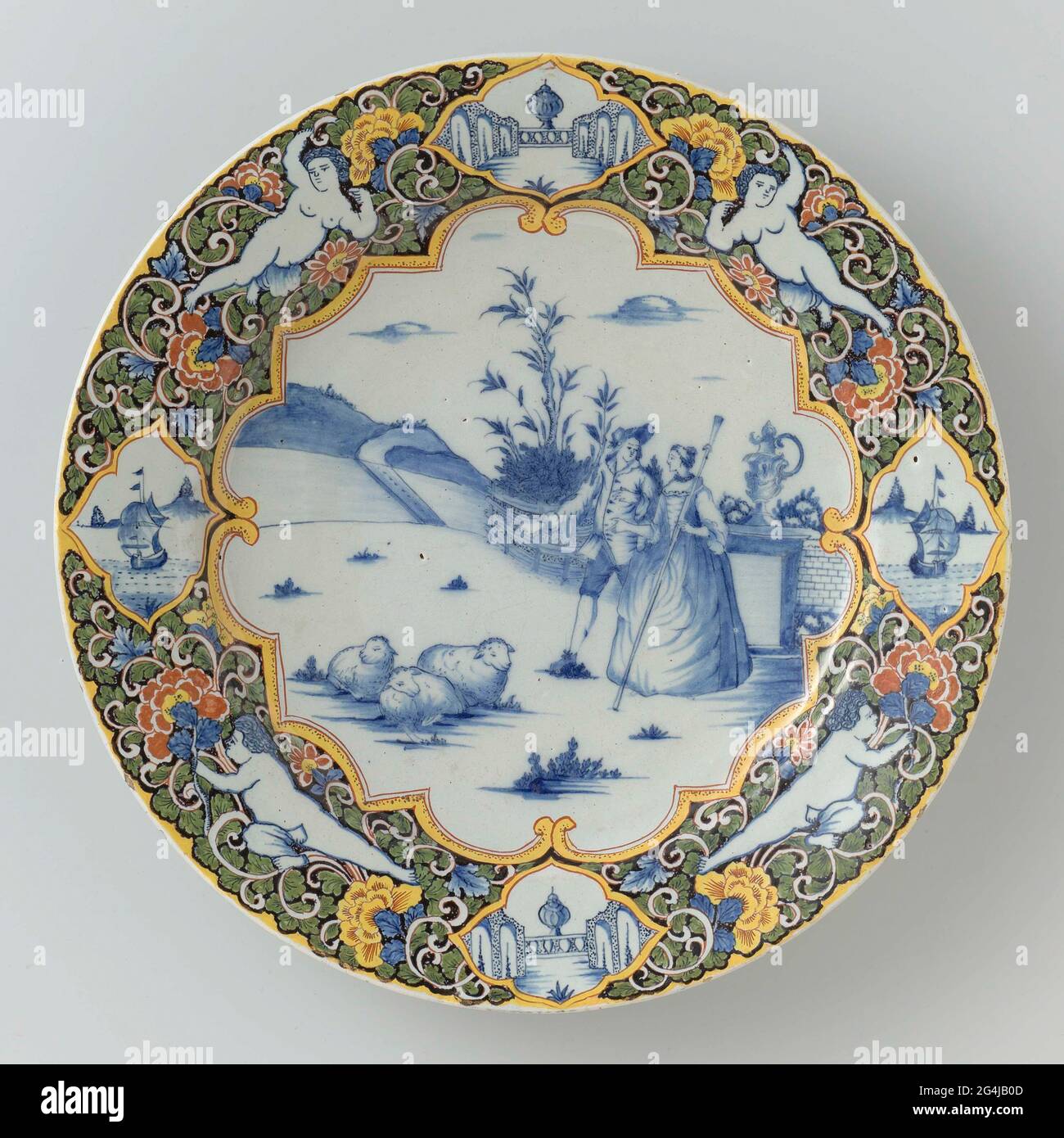 . Dish of Faïence, Dish with a shepherd scene on the flat in blue. A shepherd scene inside Louis XIV edge. Multicolored edge decoration on black ground with putti and four medallions. Stock Photo