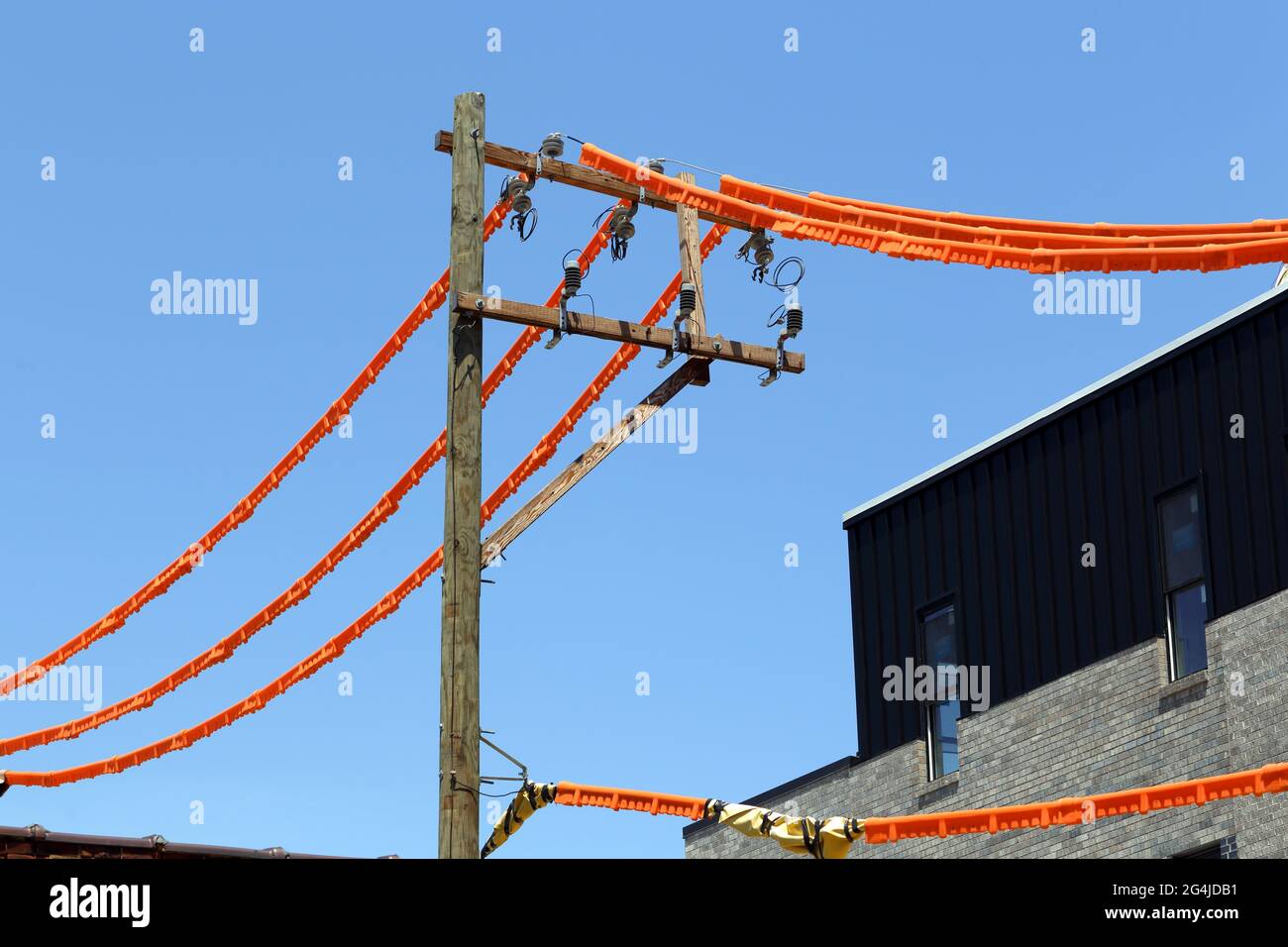 Power line covers, orange safety line guards covering electrical wires on a utility pole near a construction site as a matter of construction safety Stock Photo