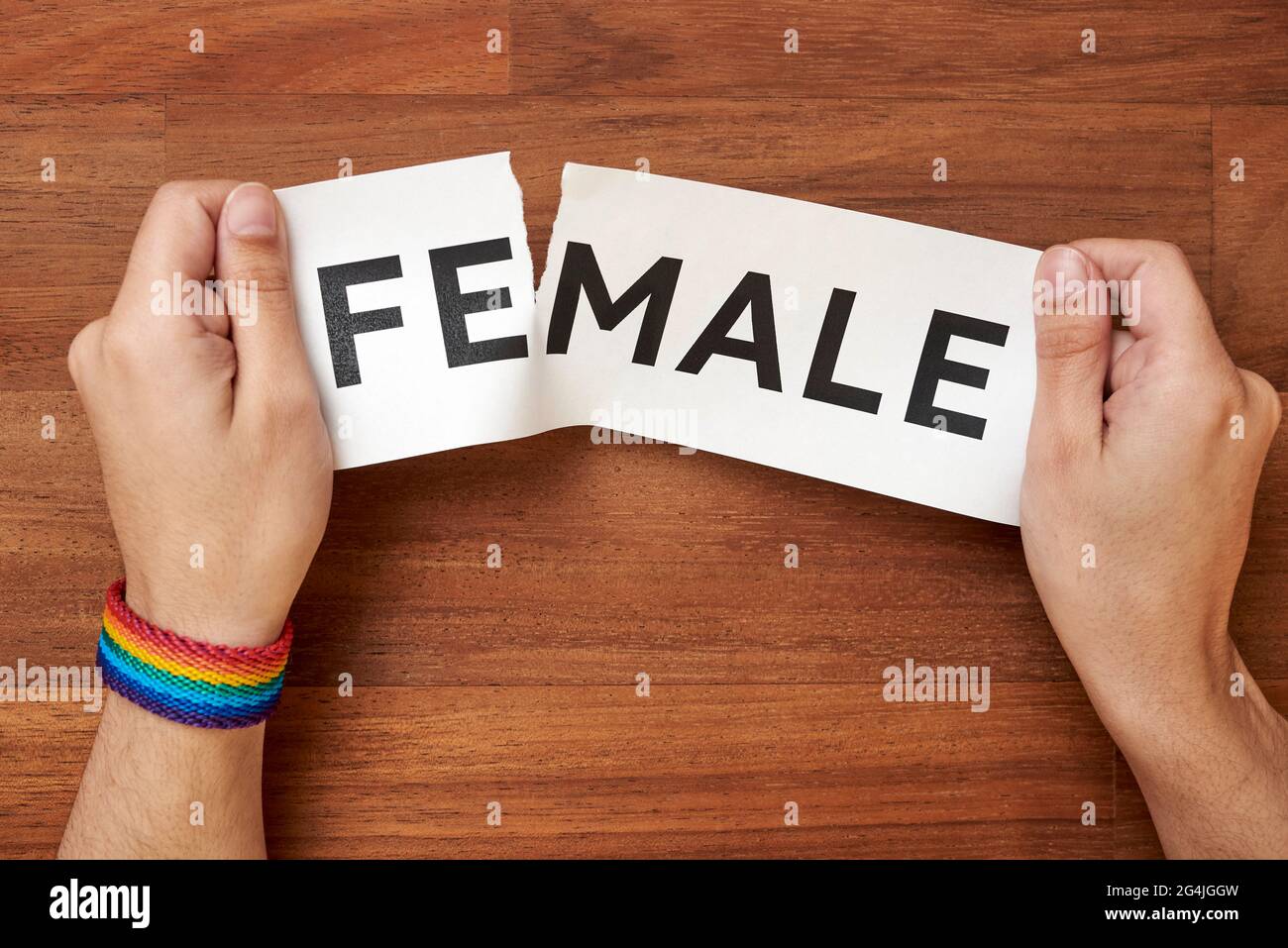 Hands ripping the word female, leaving male, wearing a rainbow bracelet, lgbt symbol. Conceptual image about gender identity and transgender. Wood bac Stock Photo