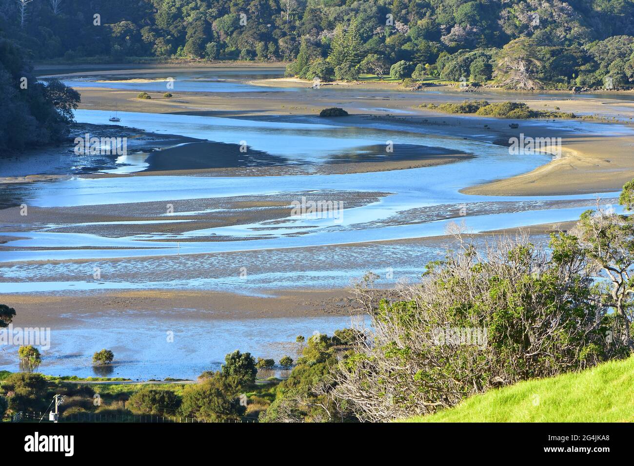 Tidal river meandering through estuary among mudflats exposed at low tide. Stock Photo
