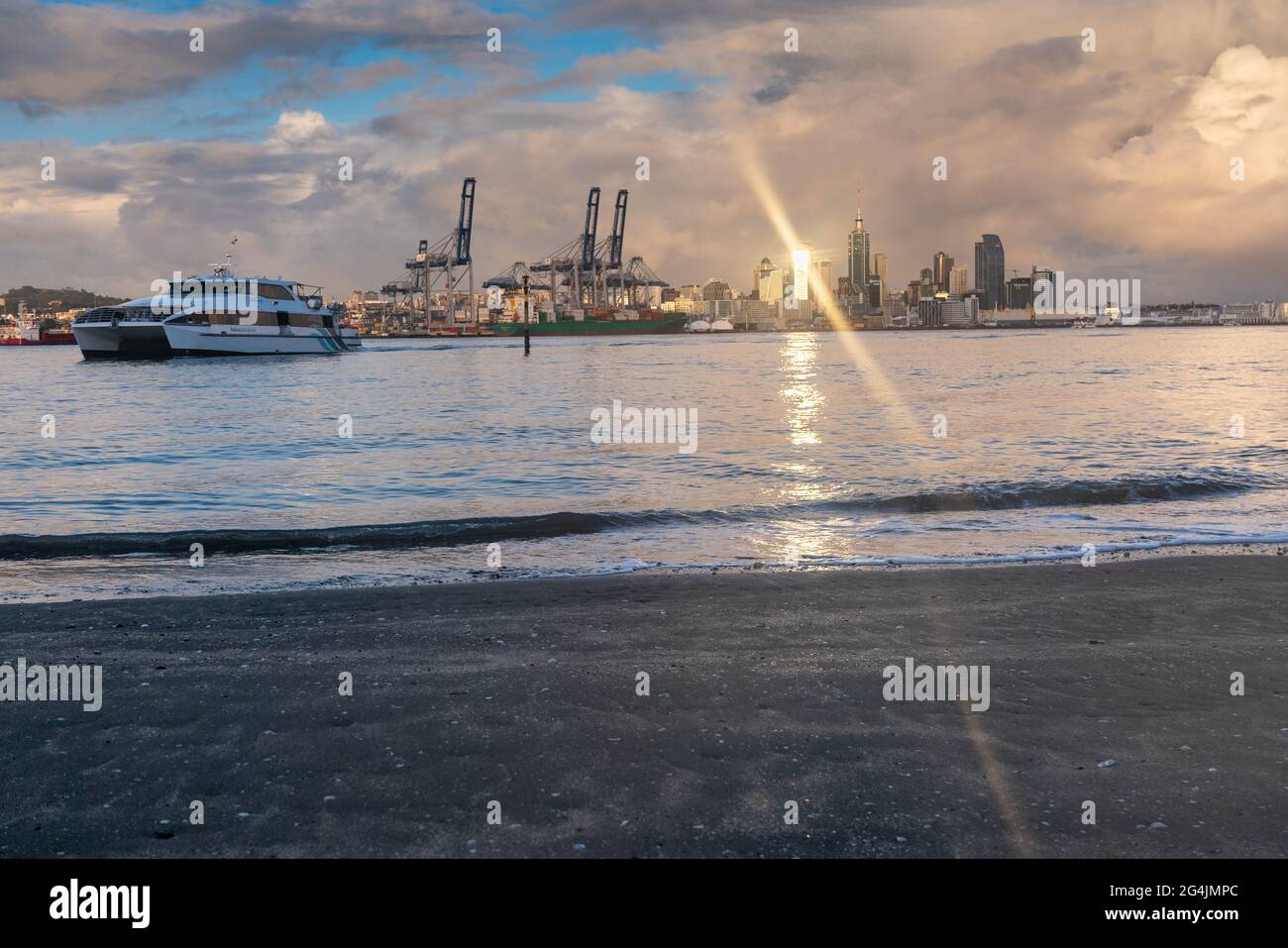 View of Auckland city buildings and skyline from across harbour at Devonport as sun rise strikes glass facades and ferry crosses delivering morning co Stock Photo