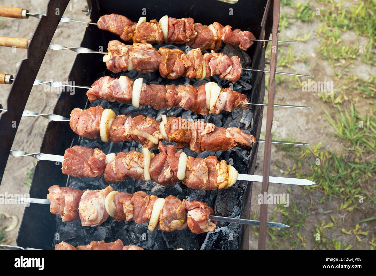 Grilling marinated shashlik preparing on a barbecue grill over charcoal.  Shashlik is a form of Shish kebab popular in Eastern Europe. Shashlyk (meaning  skewered meat) was originally made of lamb. Stock Photo