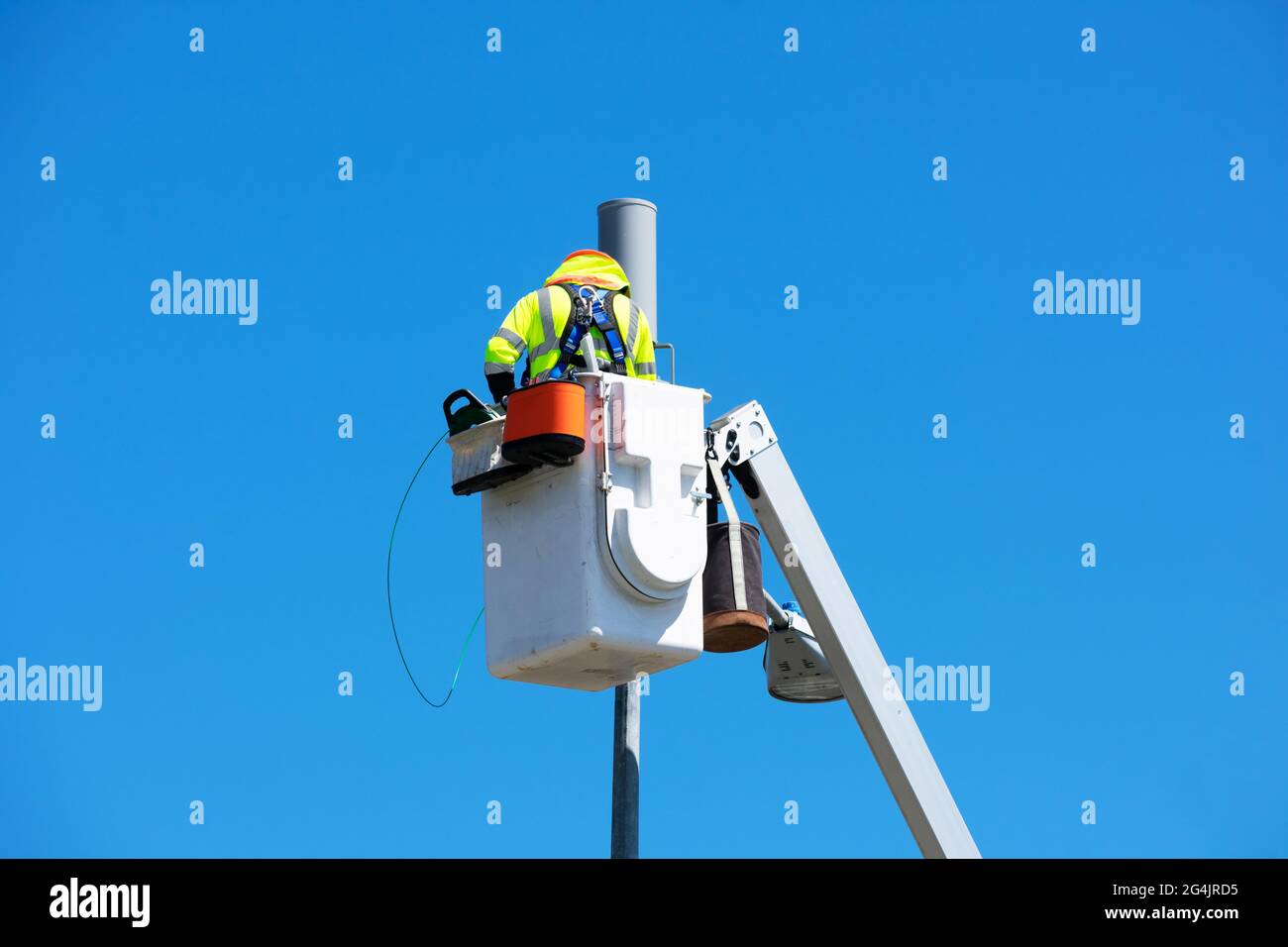 Technician works on installing or repairing a small cell antenna on a lamp post from the platform of the telescopic boom lift. Blue sky. Stock Photo