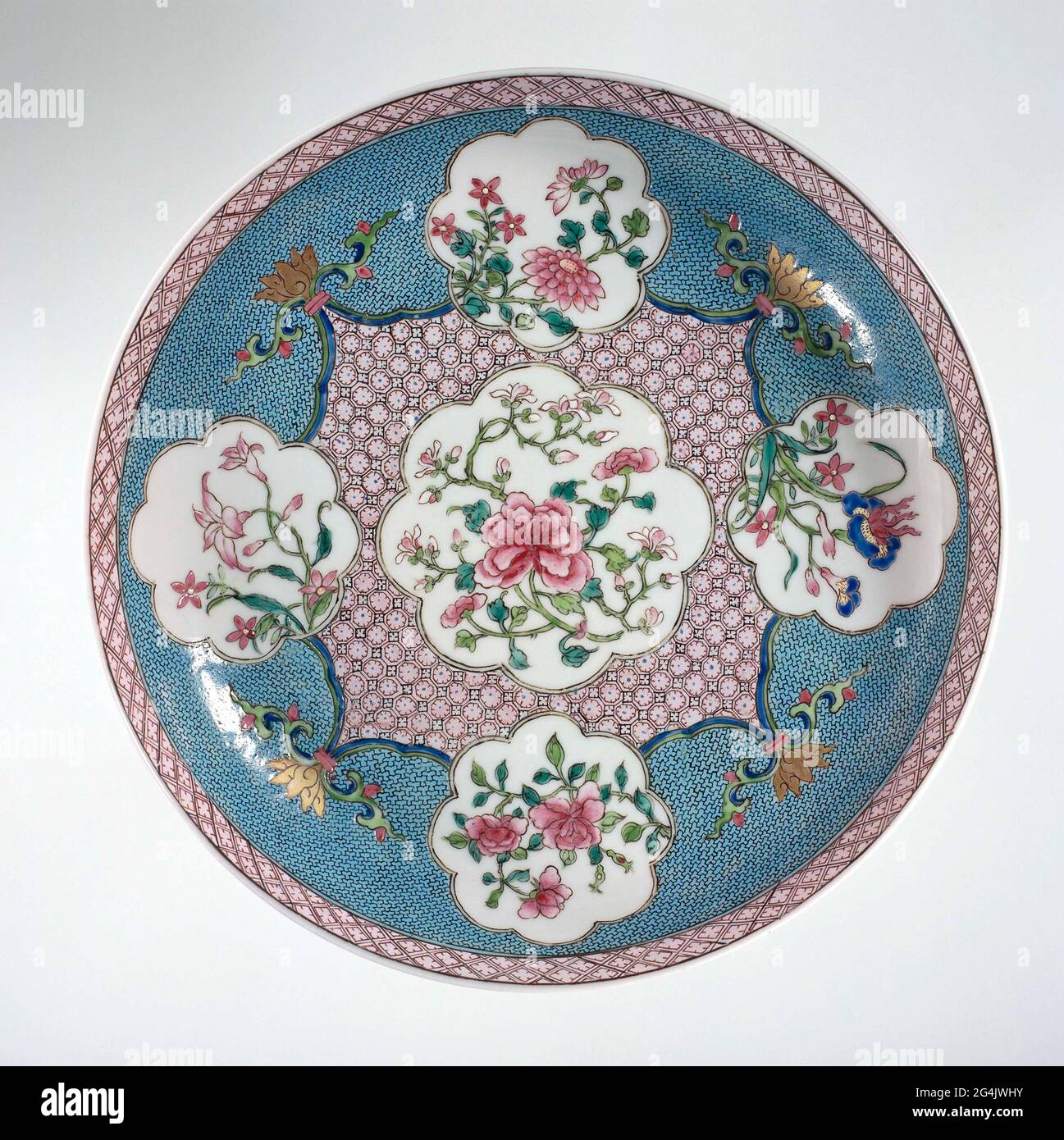 . Scale of porcelain, covered with a pink glaze and painted on the glaze in blue, red, pink, green, black and gold. On the front of the dish a lobd cartouche with a peony plant in a square scalloped cartouche with napkin, on the corners a stylized lotus drink; On each side of the square a smaller lobd cartouche with a flowering plant (peony, chrysanthemum, iris, balloon clock) against a ground of napkin; On the inner edge a band with napkin; The outside covered with a pink glaze. Famille Rose with a Ruby Back. Stock Photo