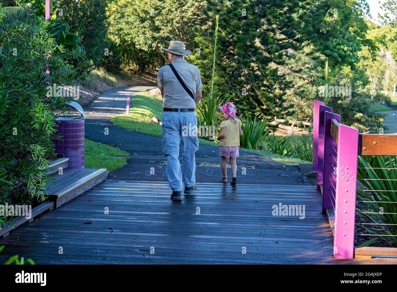 Mackay, Queensland, Australia - June 2021: Grandfather walking with his little granddaughter in the botanic gardens in early morning shadows Stock Photo