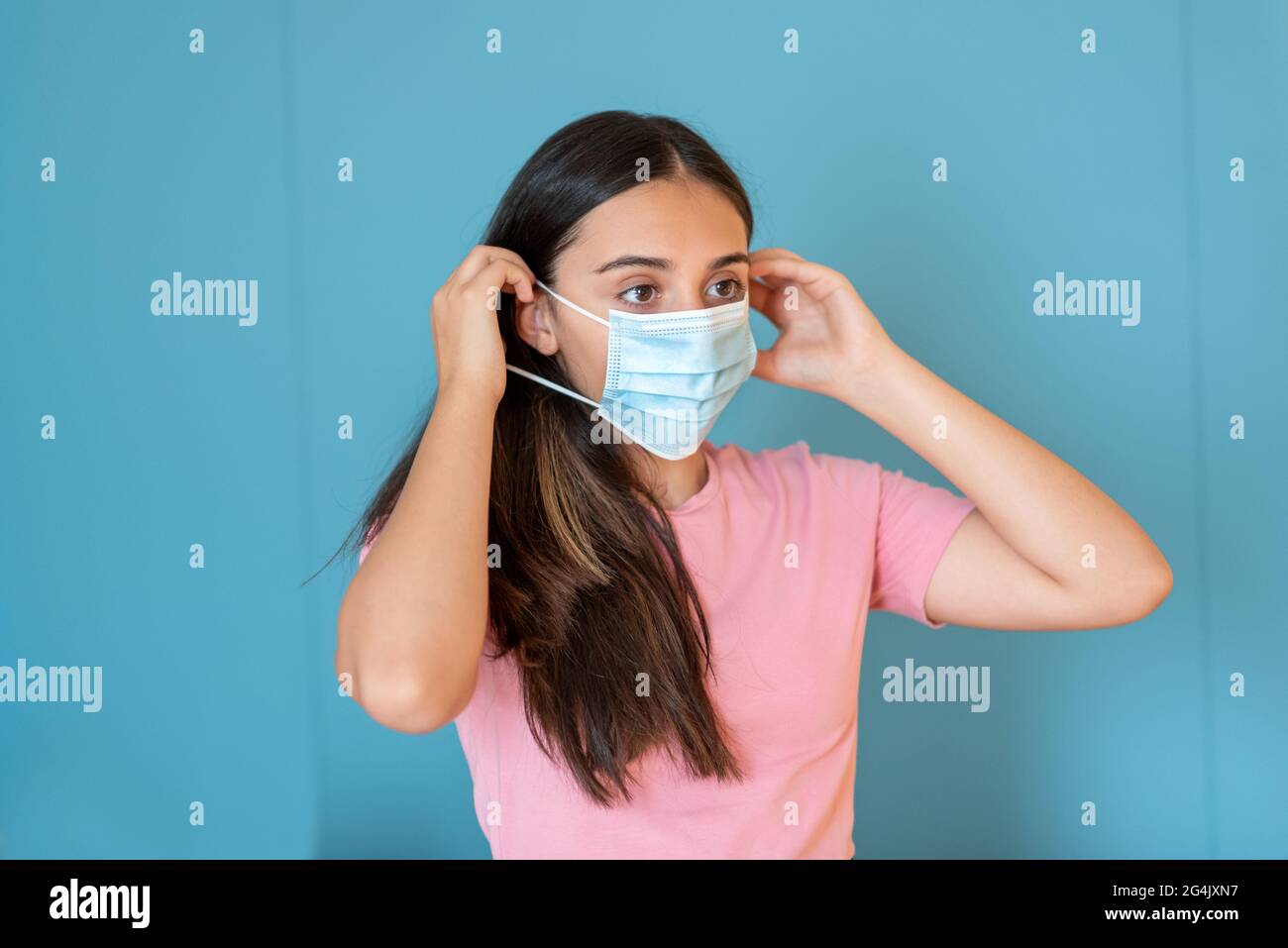 Young teenage girl wearing a disposable face mask placing the elastic behind her ears during the Covid-19 pandemic Stock Photo