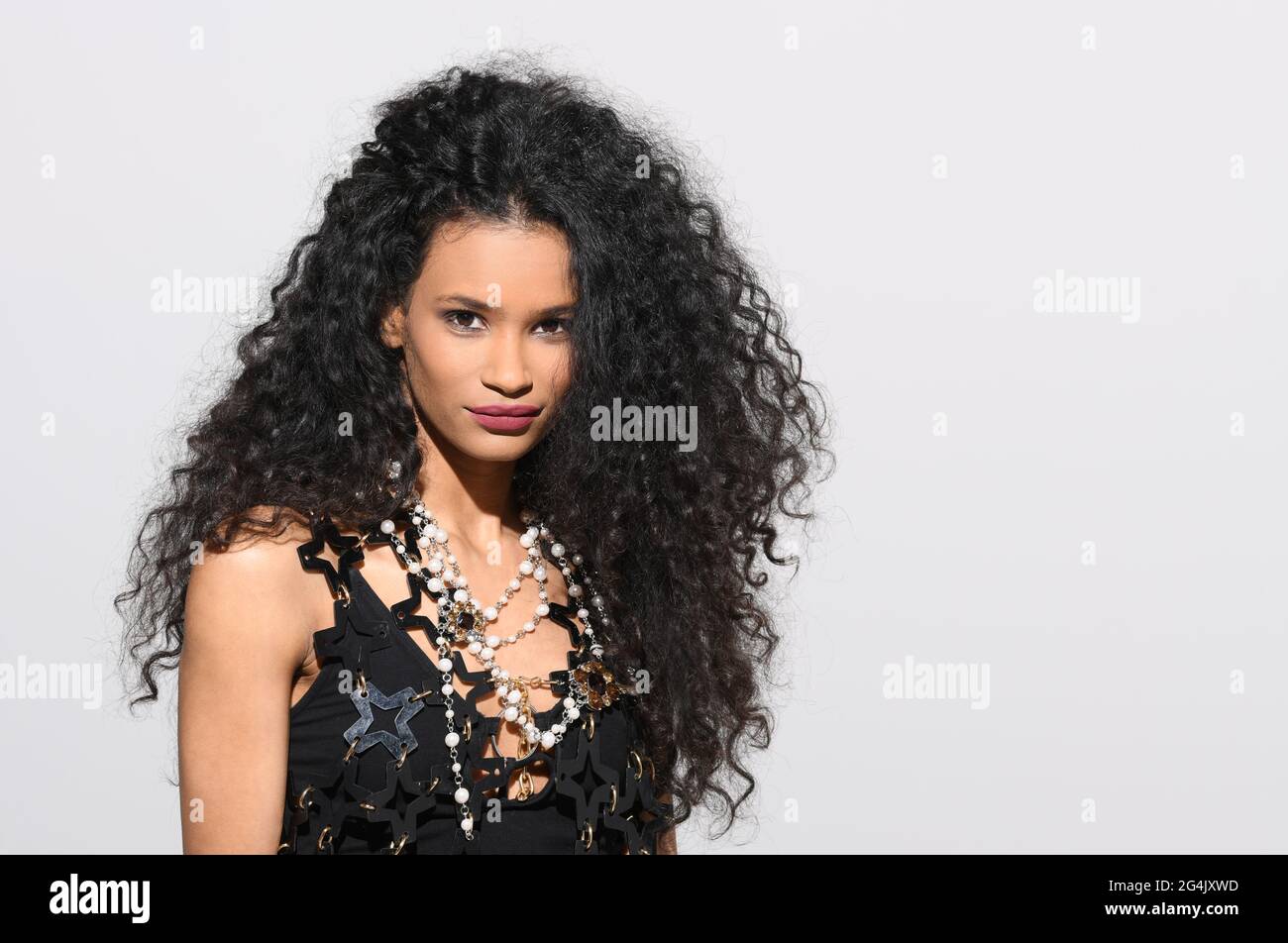 Elegant black woman in a black ensemble with pearl necklace looks into camera Stock Photo