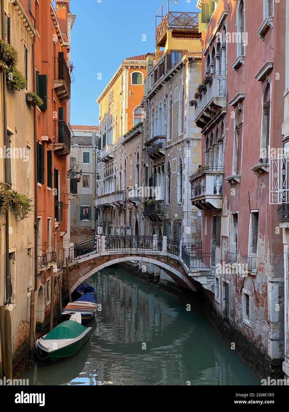 A narrow, quiet canal in Venice, Italy, lined with historic, colorful buildings and a small, arched bridge.