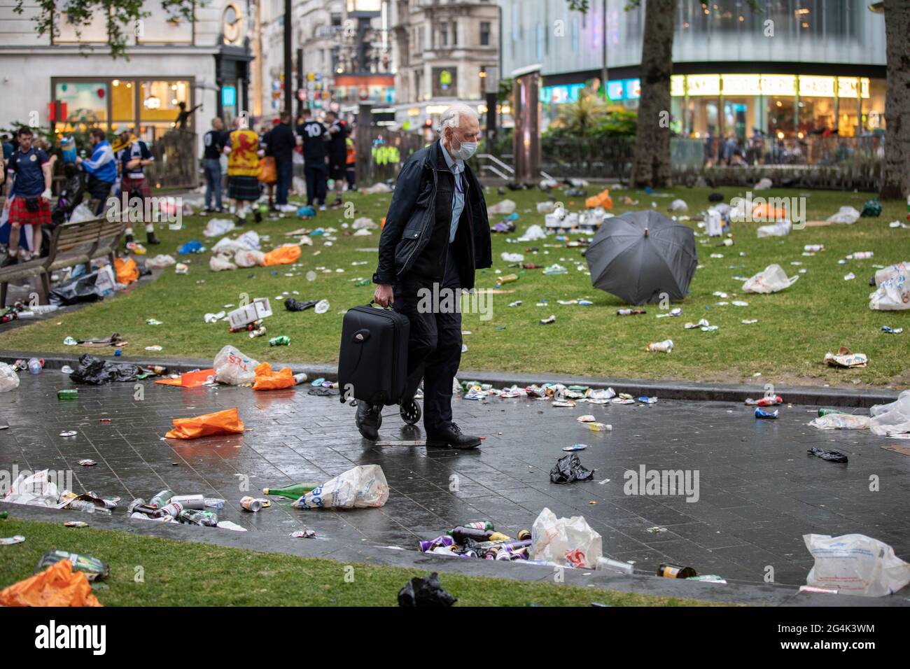 A man carrying his travel suitcase makes his way through all the  broken bottles and rubbish left behind by Scottish football fans in Leicester Square Stock Photo