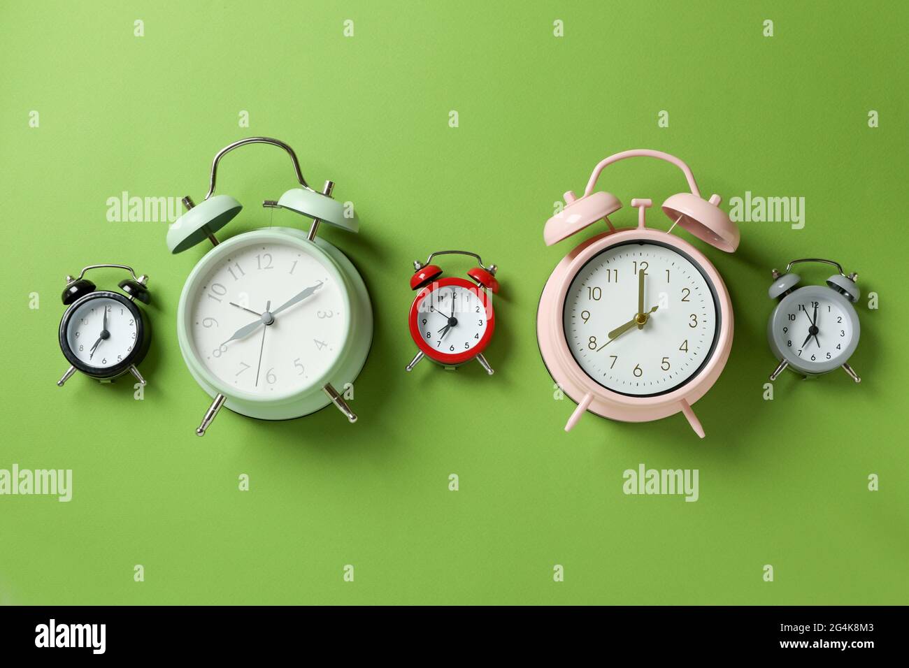 Different multicolor alarm clocks on green background Stock Photo Alamy