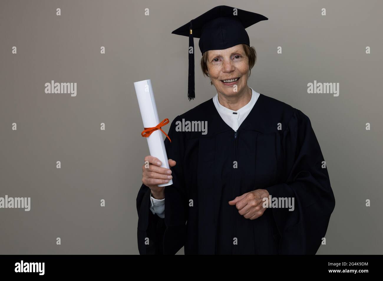 smiling older woman graduate in graduation gown holding diploma Stock Photo
