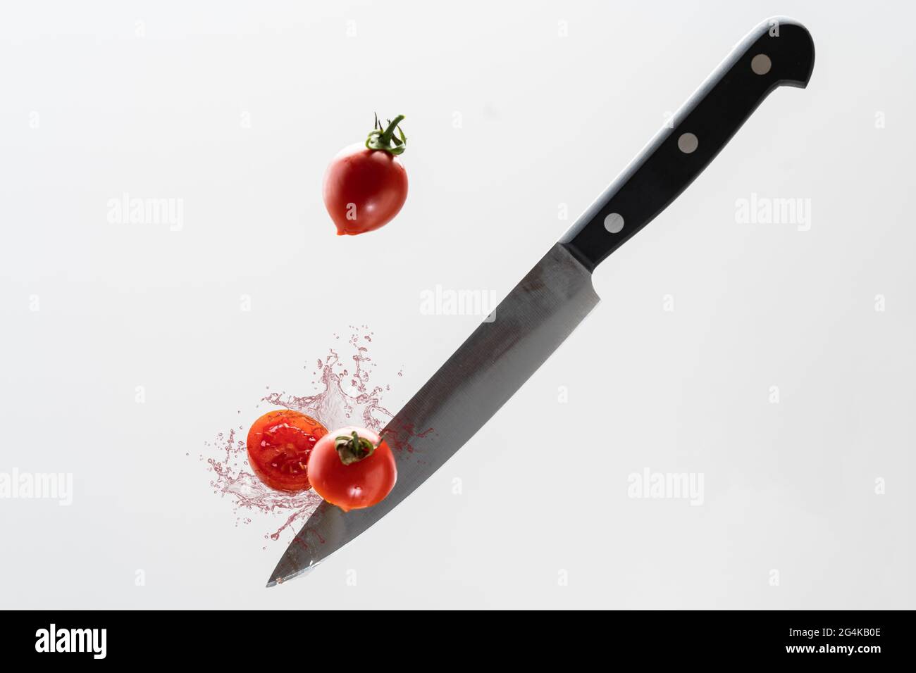 A flying knife cutting tomato with splash on white background Stock