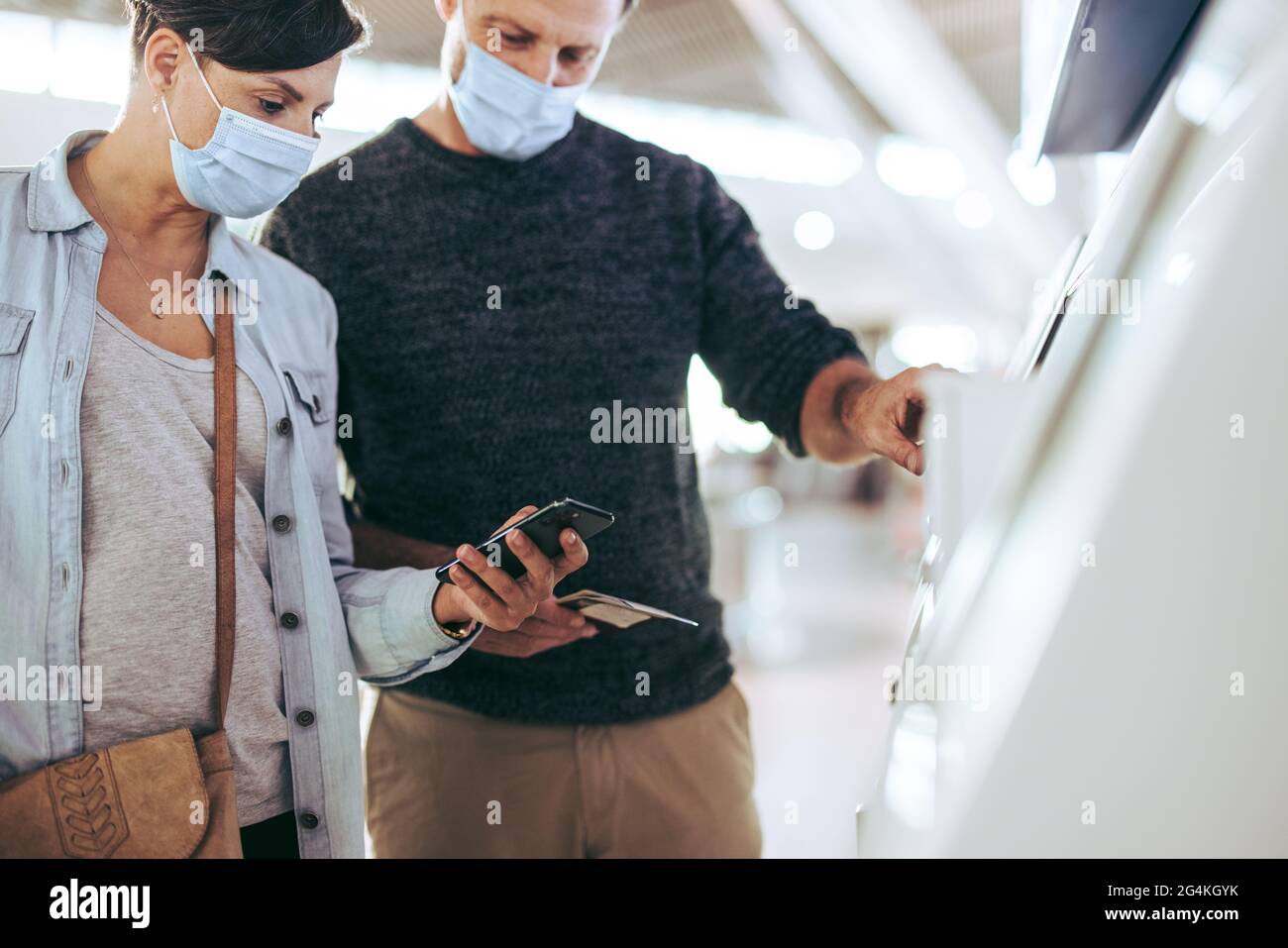 Couple putting details in self service checkin machine at airport in pandemic. Tourist family