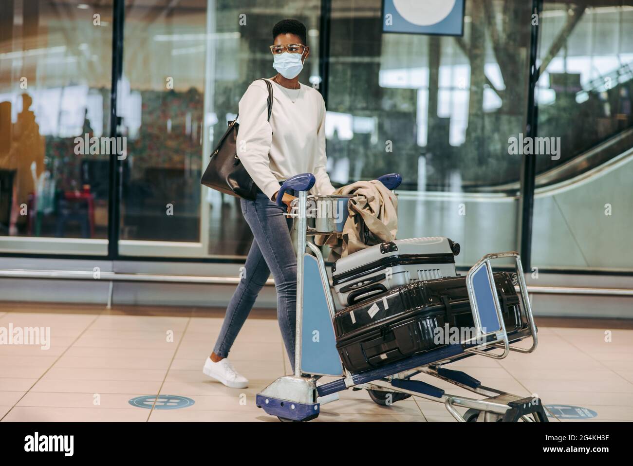 Female traveler at airport terminal with luggage trolley during