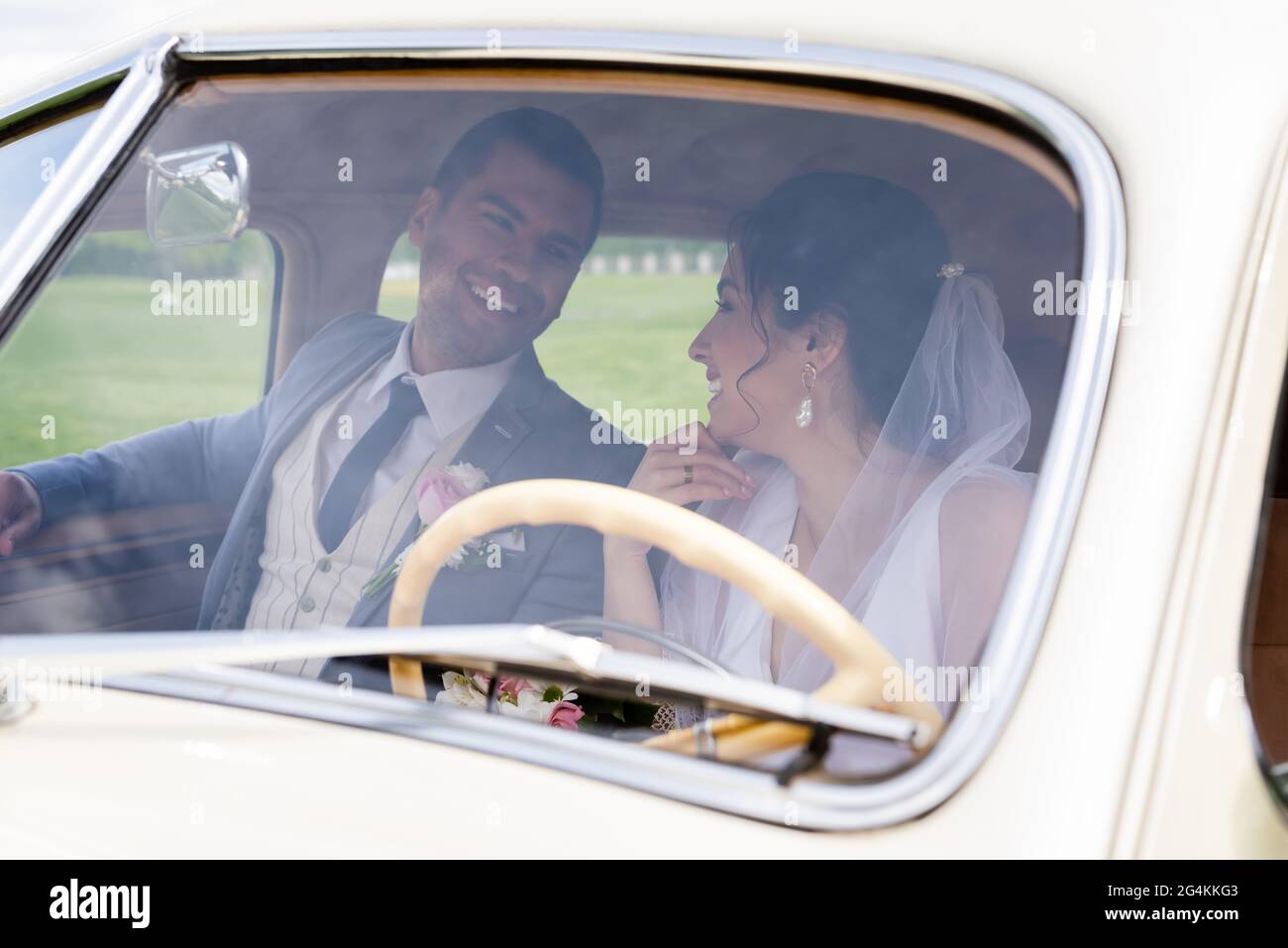 Cheerful bride and groom looking at each other in retro car Stock Photo ...