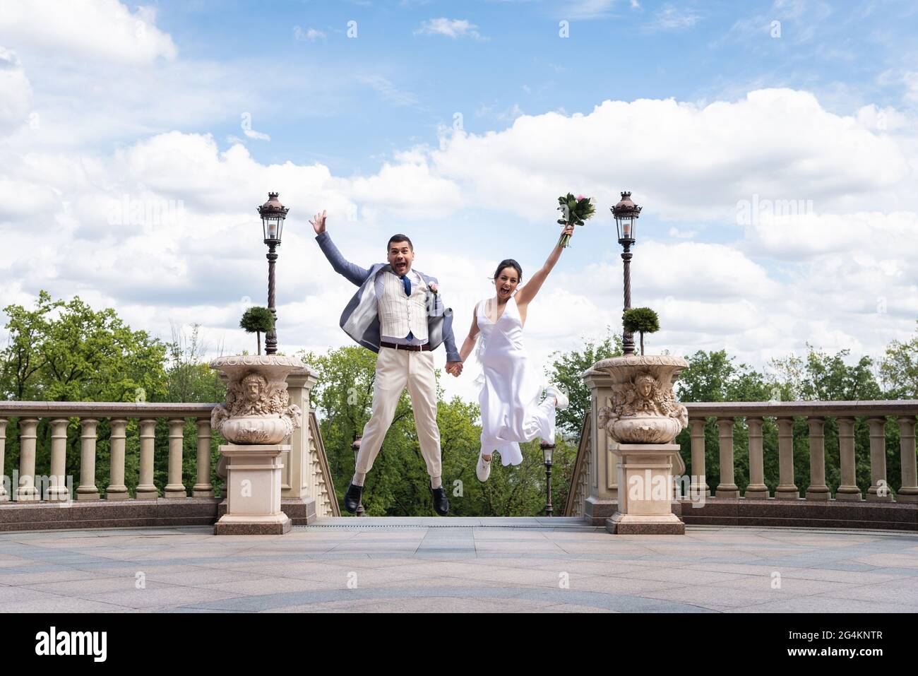 Happy newlyweds with bouquet jumping in park Stock Photo - Alamy