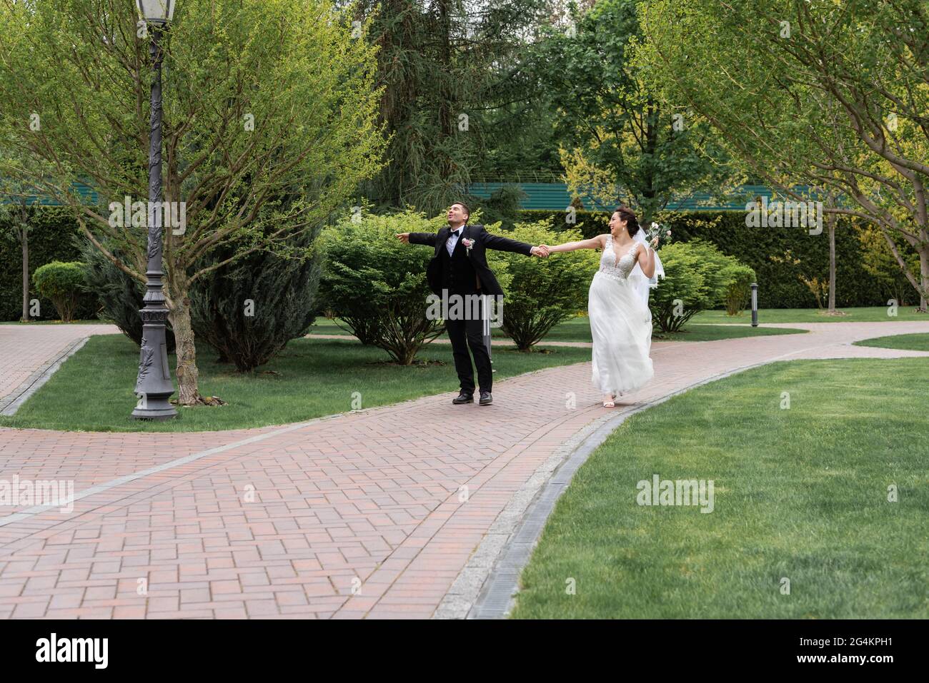 Happy newlyweds with bouquet walking in park Stock Photo - Alamy