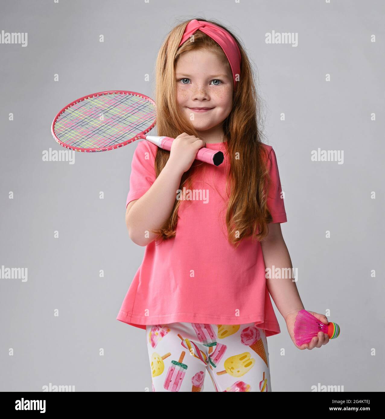 Happy smiling kid girl in pink clothes holds a badminton racquet on her shoulder and shuttlecock in hand Stock Photo