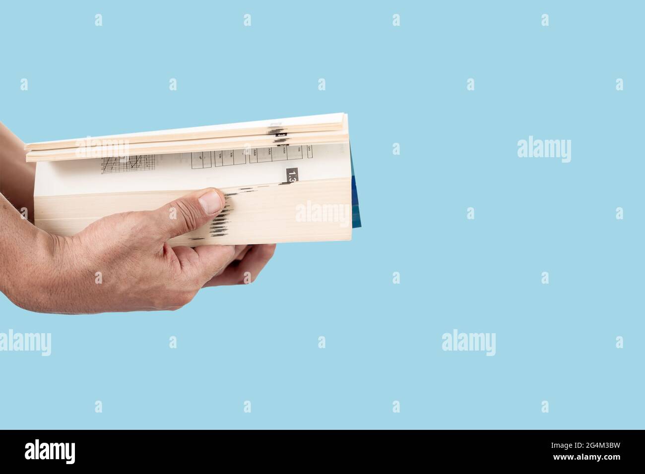 Close-up of man's hand holding and opening a thick book isolated on blue pastel color background. Stock Photo