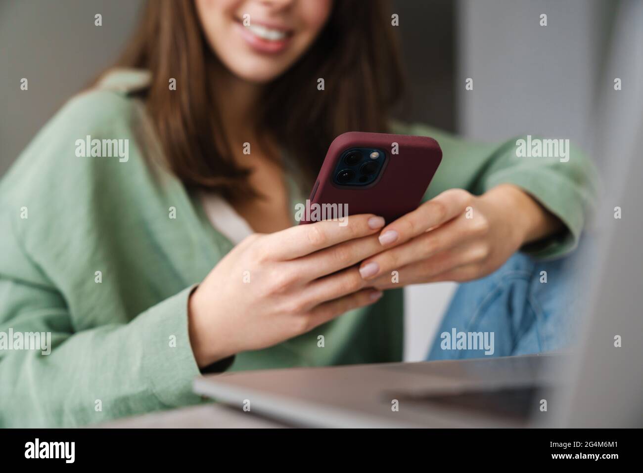 Cheerful beautiful woman using mobile phone while working with laptop at home Stock Photo