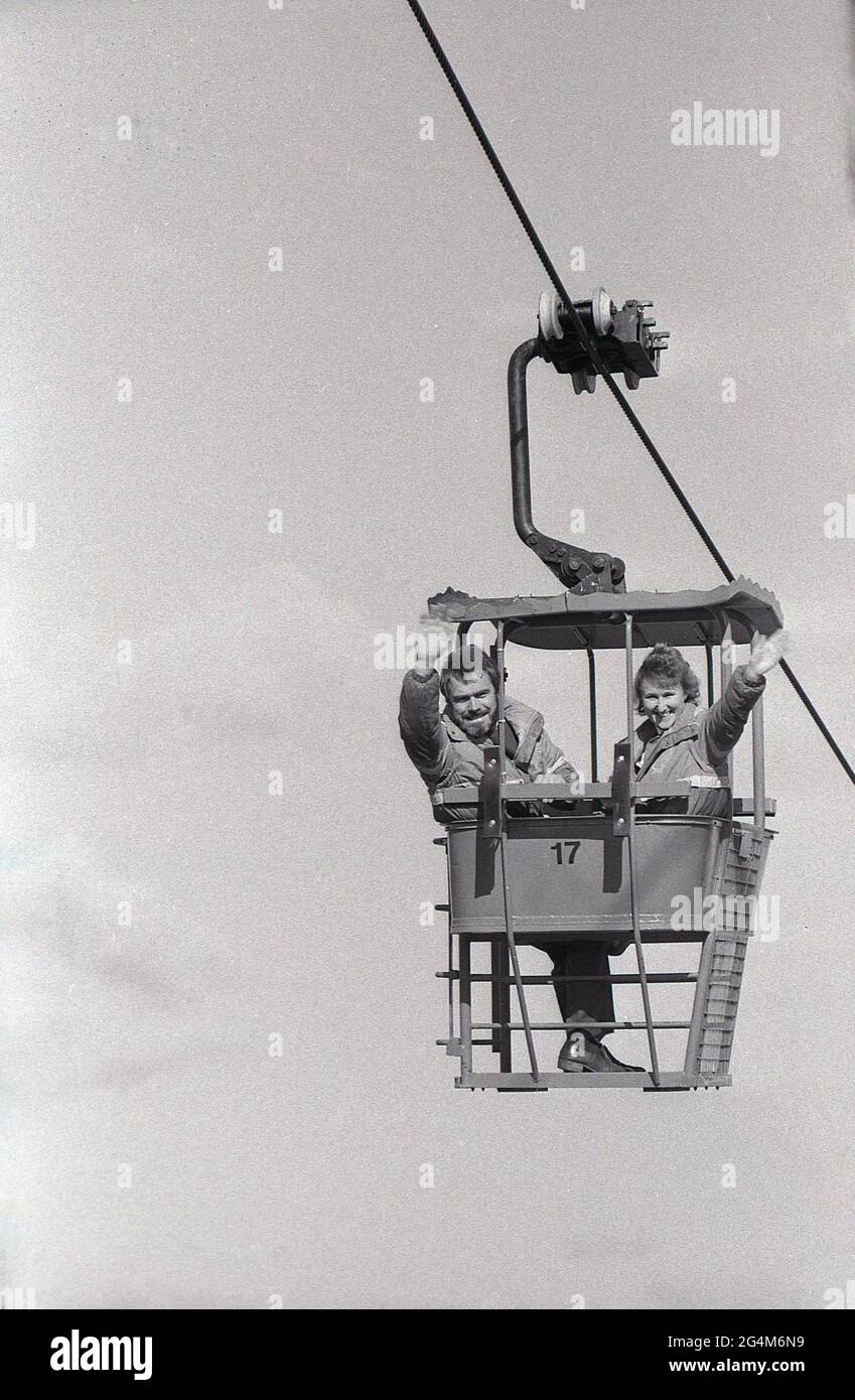 1980s, historical, a man and woman riding in a new ski or chair lift at an  outdoor artifical or dry ski slope, Yorkshire, England, UK. The two-person  double chair was the most