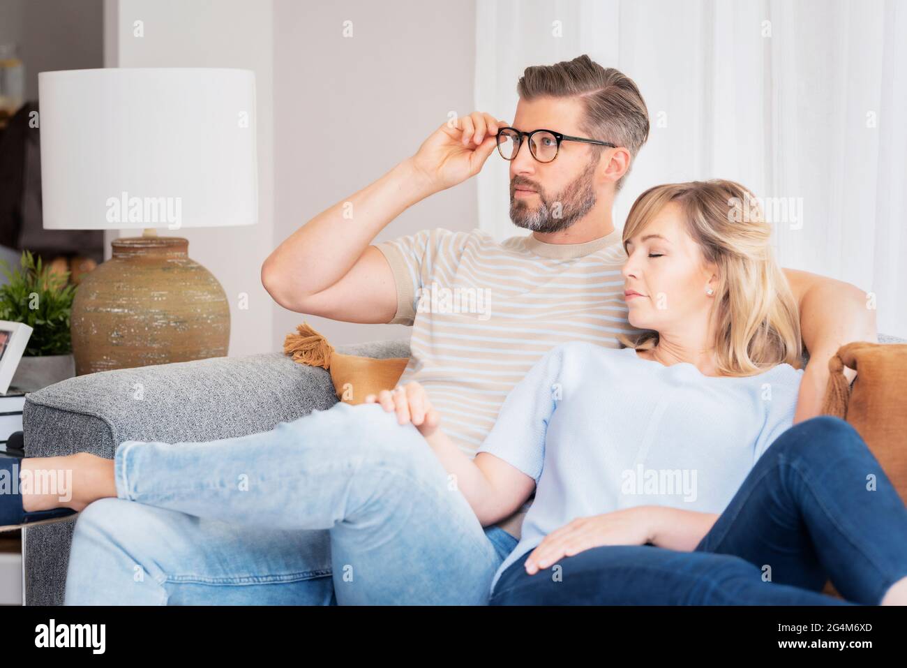 Shot of an affection couple relaxing together in their living room at home. Handsome man watching tv while her beautiful wife napping next to him. Stock Photo