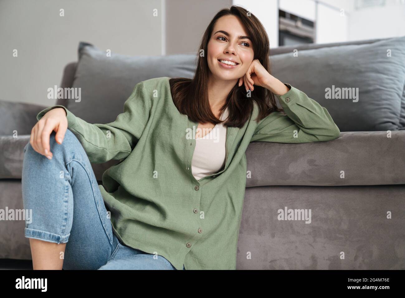 Cheerful beautiful woman smiling at camera while sitting on floor at ...