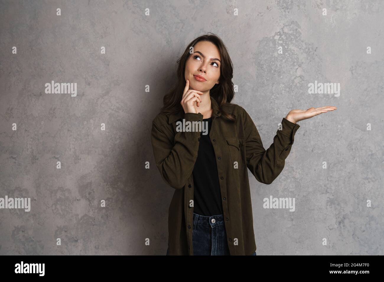 Thinking beautiful brunette girl looking upward and holding copyspace ...