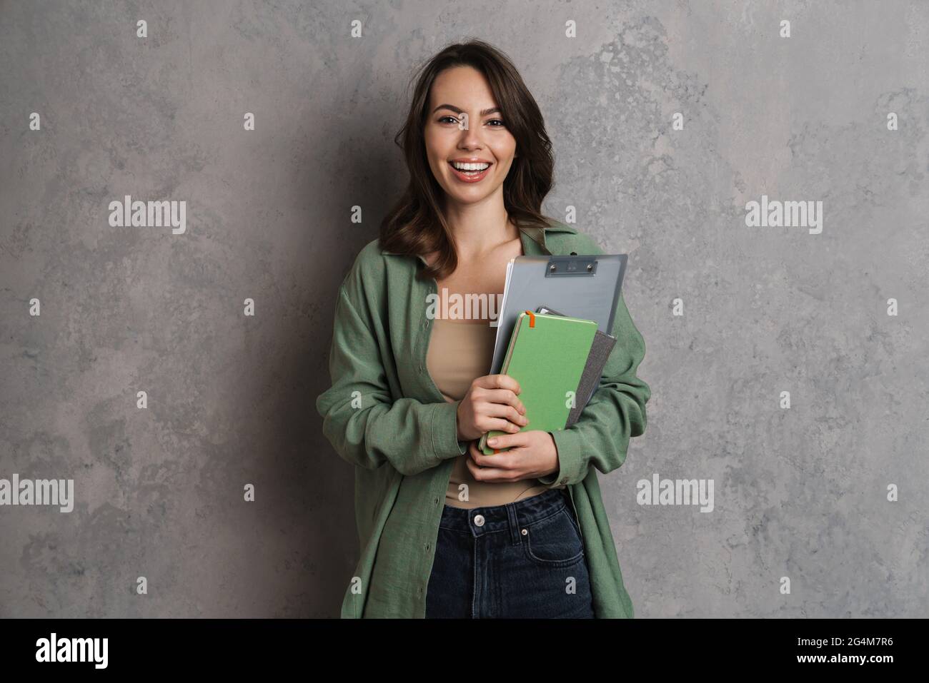Happy nice girl smiling while posing with clipboard and planners isolated over grey wall Stock Photo