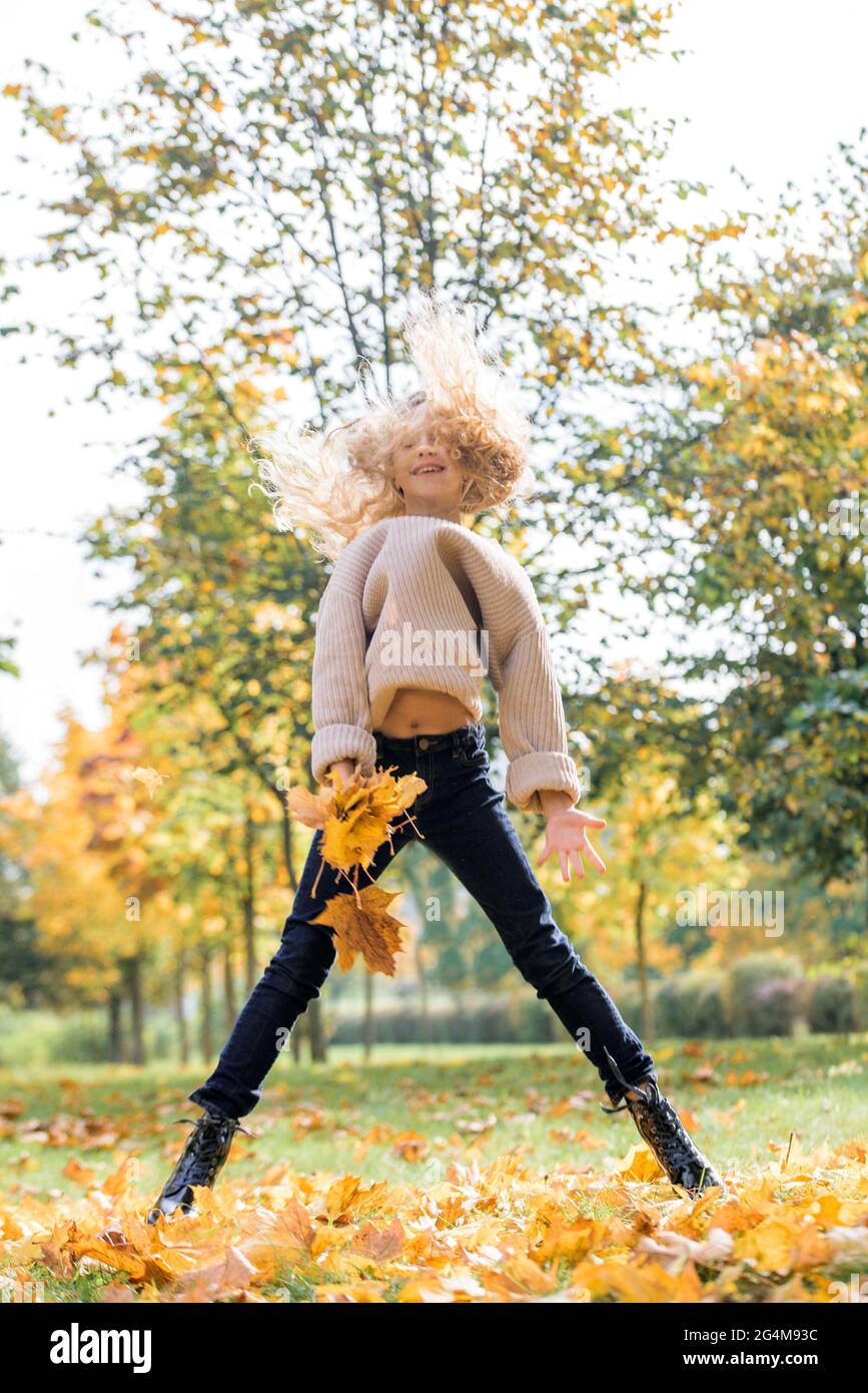 Beautiful little girl jumping with autumn leaves in the park outdoor ...