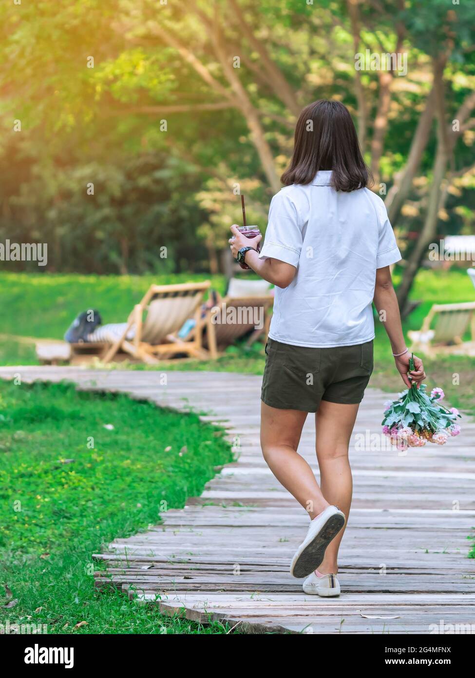 Back view of Asian woman with beverage and bouquet walk alone on ...