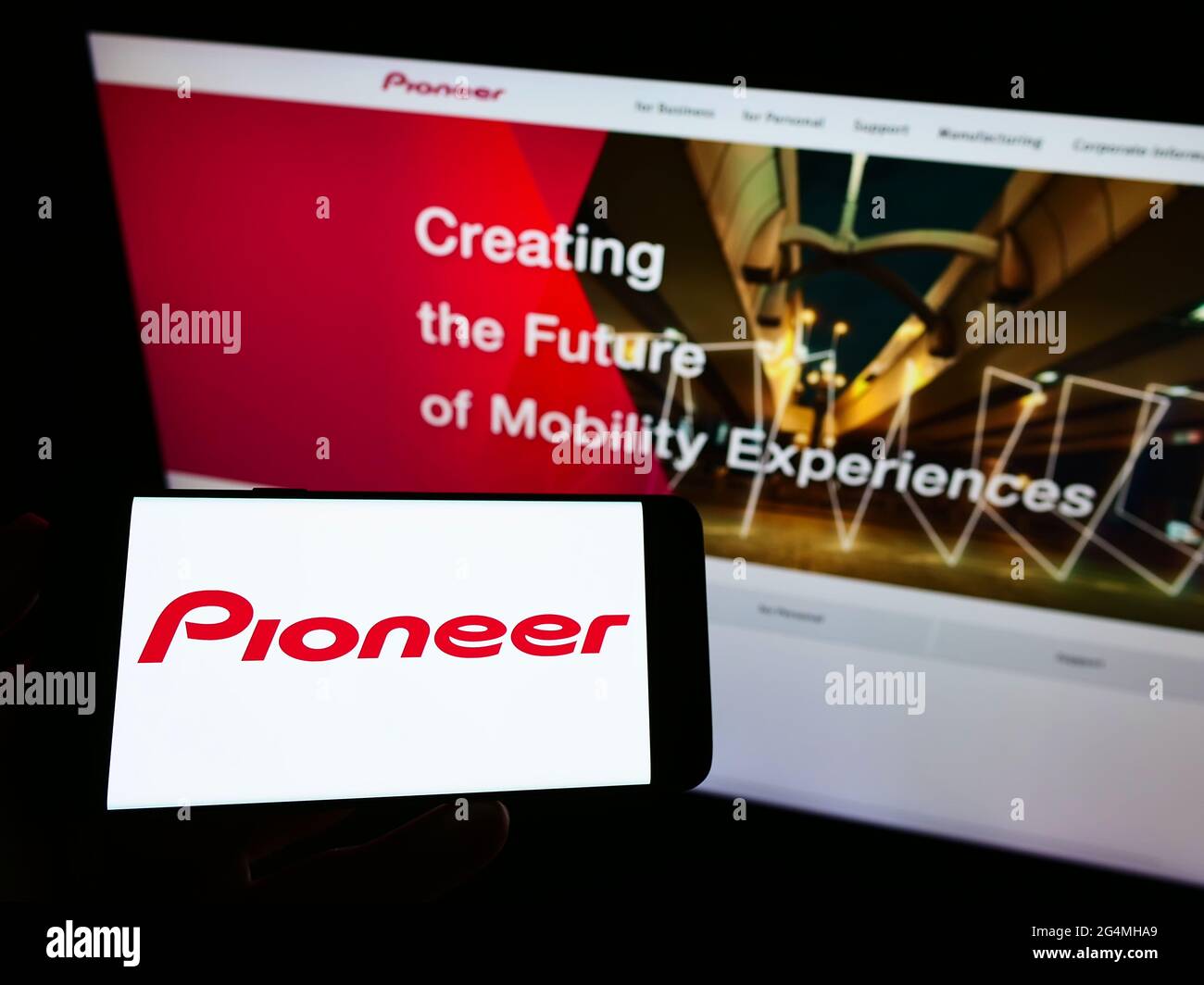 Person holding mobile phone with logo of Japanese electronics company Pioneer K.K. on screen in front of business web page. Focus on phone display. Stock Photo