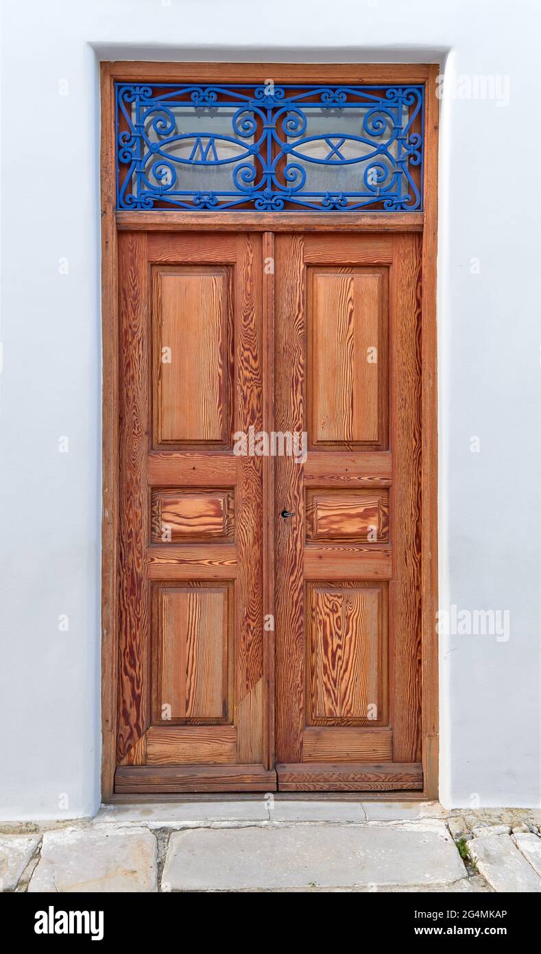 Old vintage wooden doors in light natural color decorated with blue forge-smithing metal ornament with monograms of capital letters M and X Stock Photo