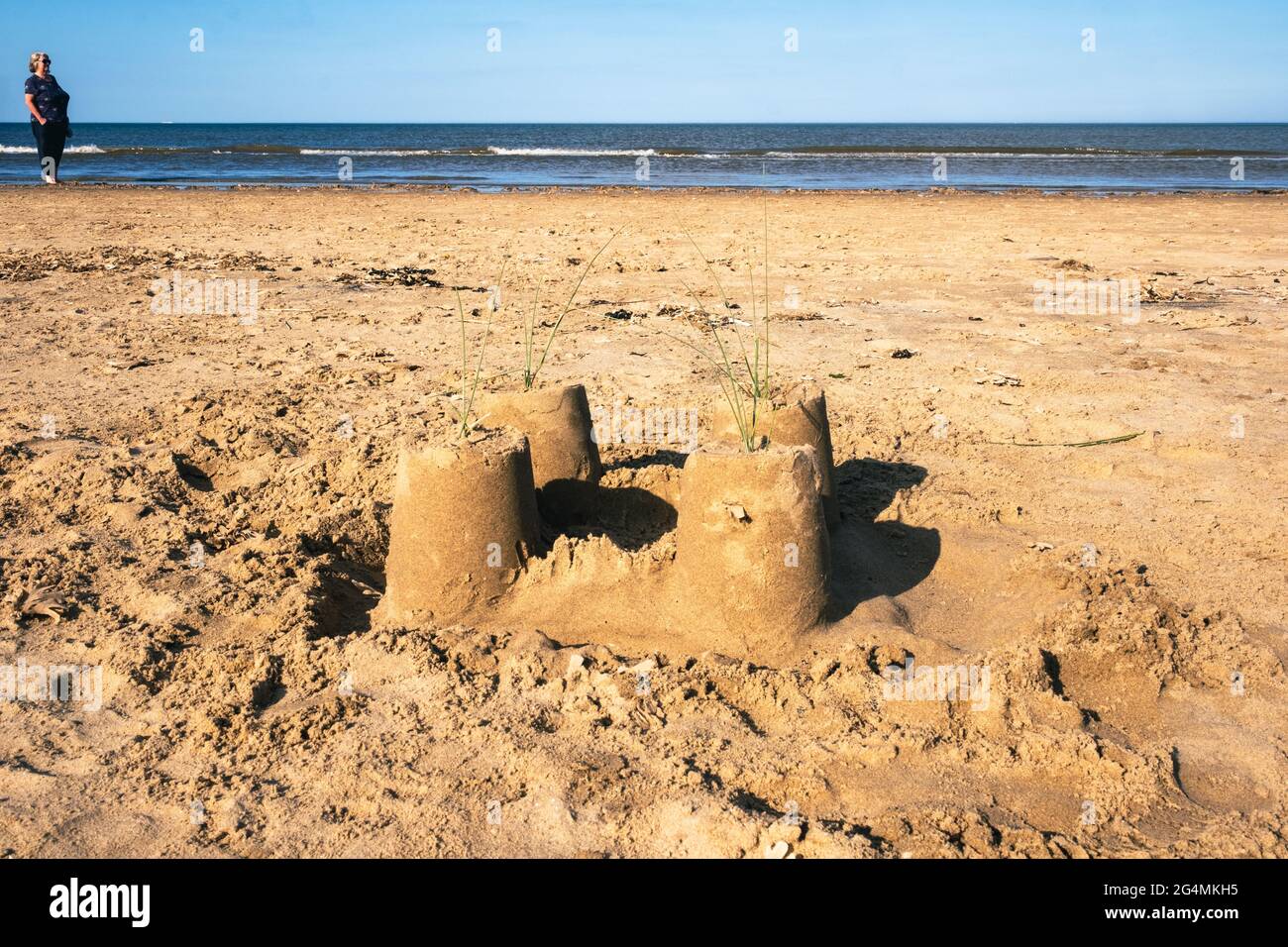 An abandoned sandcastle on the north beach of Mablethorpe in Lincolnshire with a woman in the distance looking along the shoreline, on a hot summer da. Stock Photo
