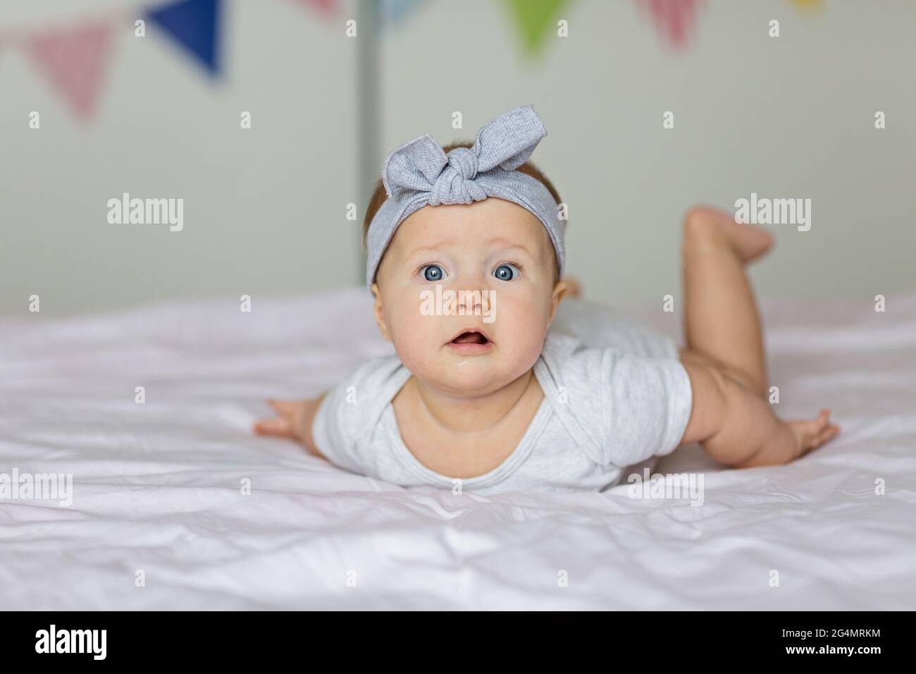 Caucasian blonde baby six months old lying on bed at home. Kid wearing