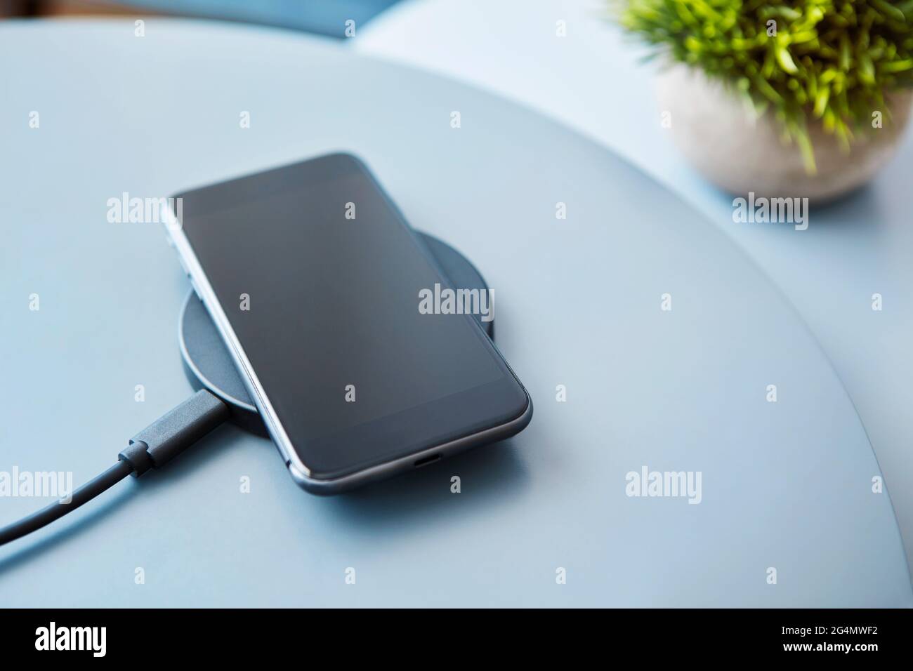 Wireless inductive charging smartphone battery. Electronic communication device against light blue background. Modern technology, wireless device and Stock Photo