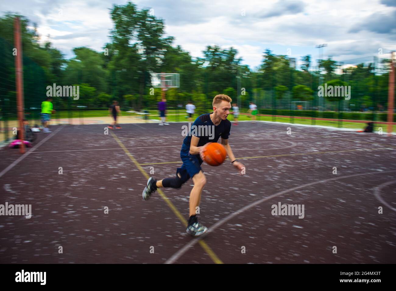 Young redhead guy running and dribbling a basketball at high speed on a sports field on the street during the day motion blurred Stock Photo