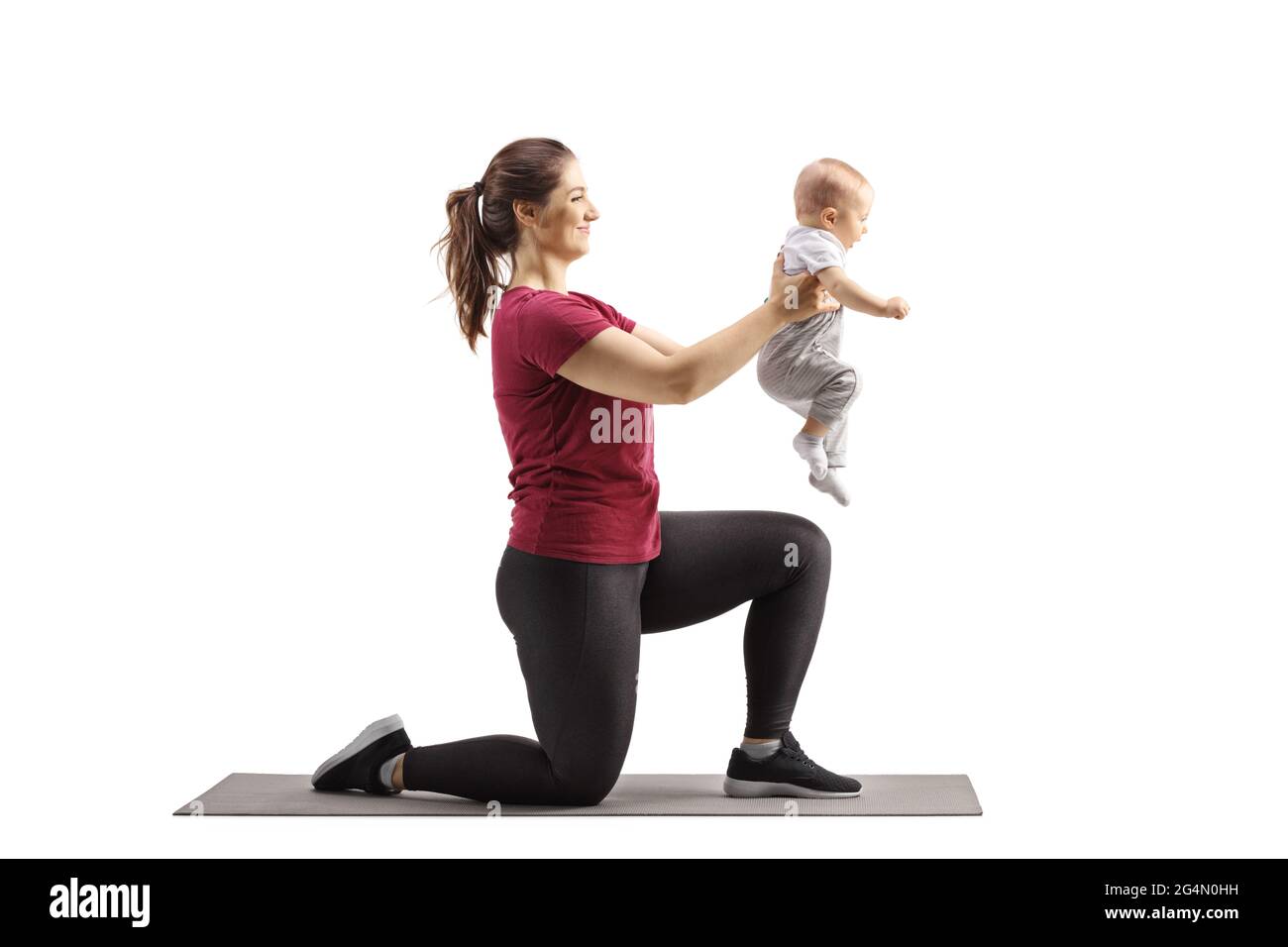 Young mother kneeling on an exercise mat and holding her baby isolated on white background Stock Photo