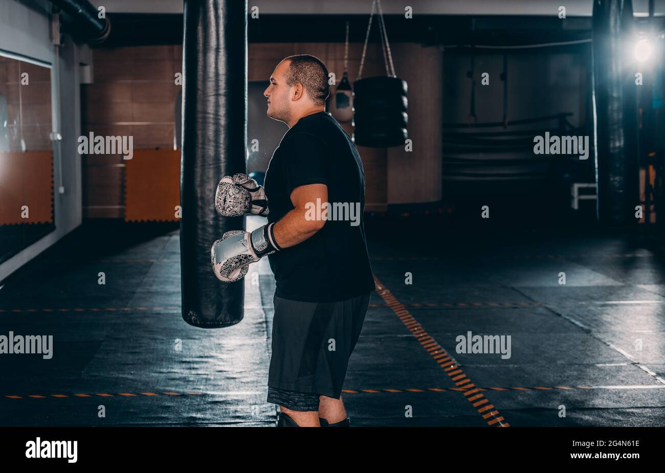 Young muscle boxer using a punching bag in gym. Boxer hitting punching