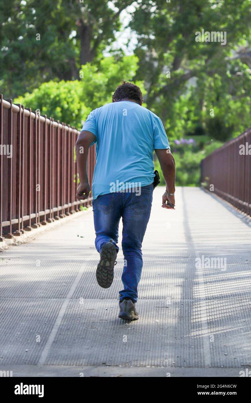 A rear view of a male person running on a footbridge against a blurred ...