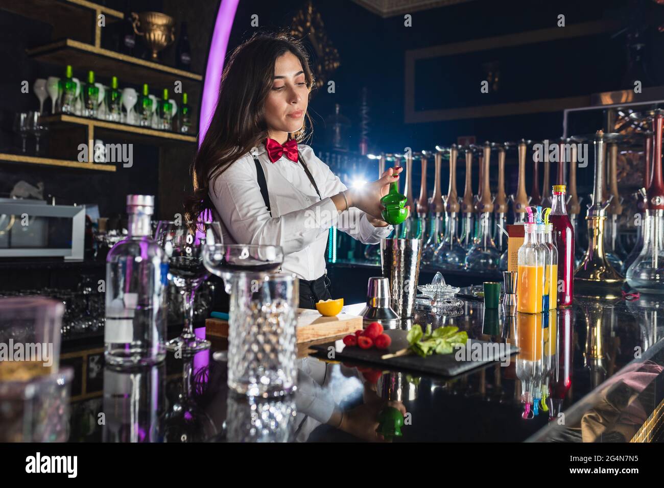 Young female barkeeper in stylish outfit squeezing lemon while preparing cocktail standing at counter in modern bar Stock Photo