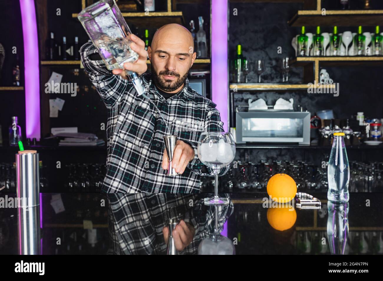 Focused male barkeeper adding liquid from bottle into jigger while preparing cocktail standing at counter in modern bar Stock Photo
