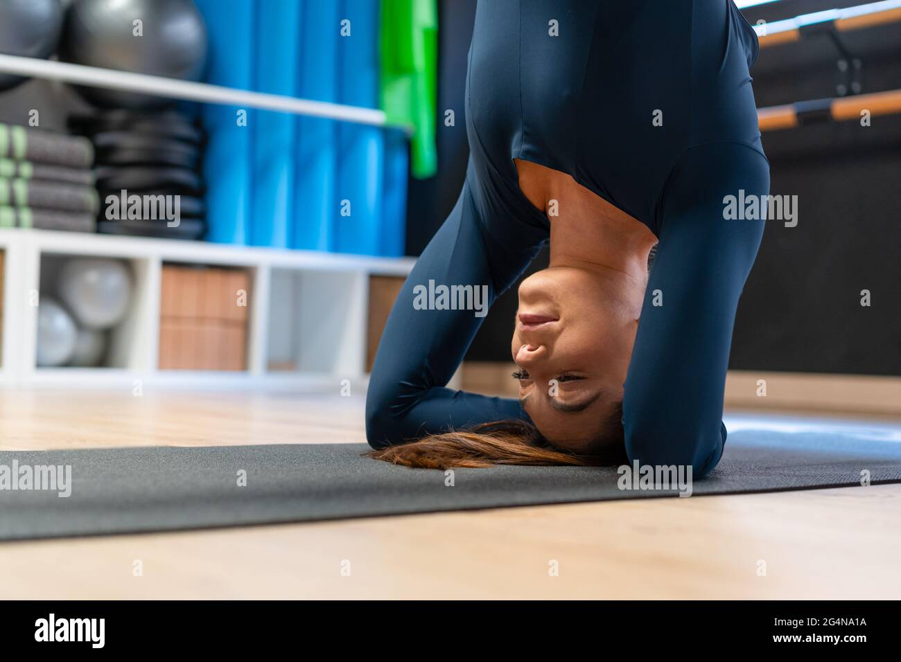 Fit female in sportswear doing supported headstand variation pose while practicing yoga in fitness studio Stock Photo