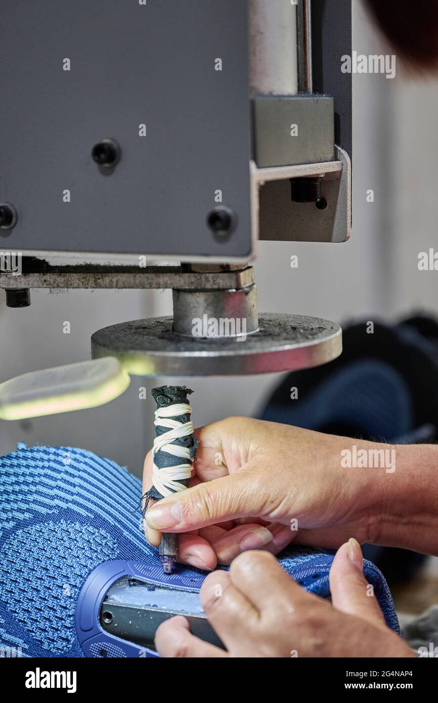 Detail of worker making holes for shoelaces at Chinese shoes factory Stock Photo