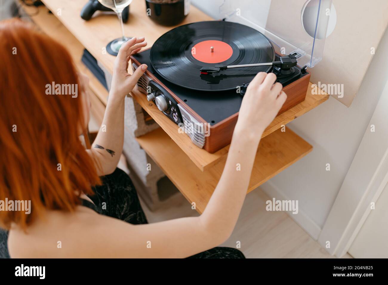 From above side view of crop anonymous female turning on retro record player on shelf in house Stock Photo