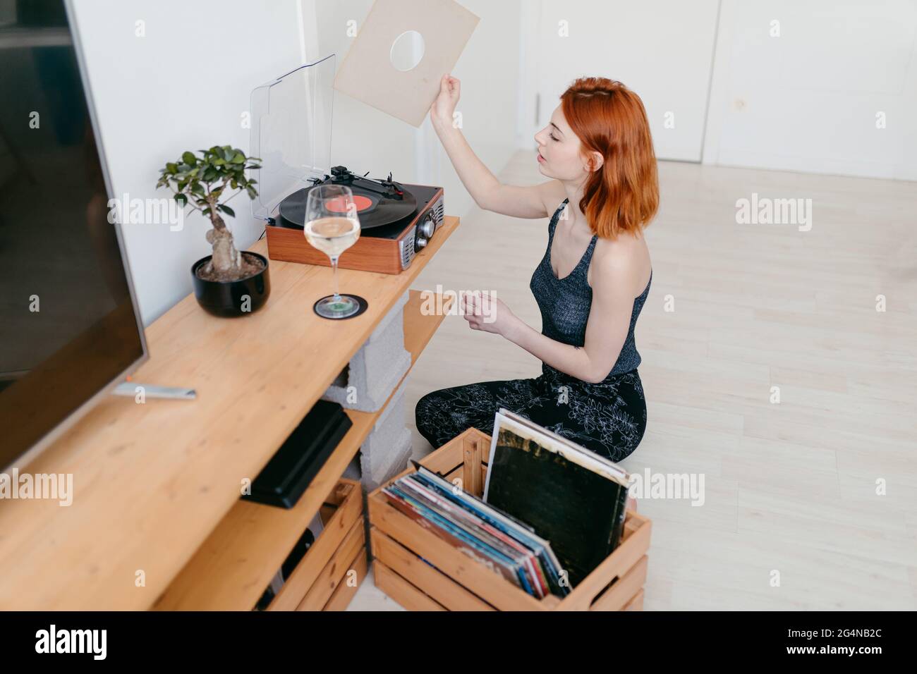 Young female selecting vinyl record from wooden container while sitting against vintage turntable in house room Stock Photo