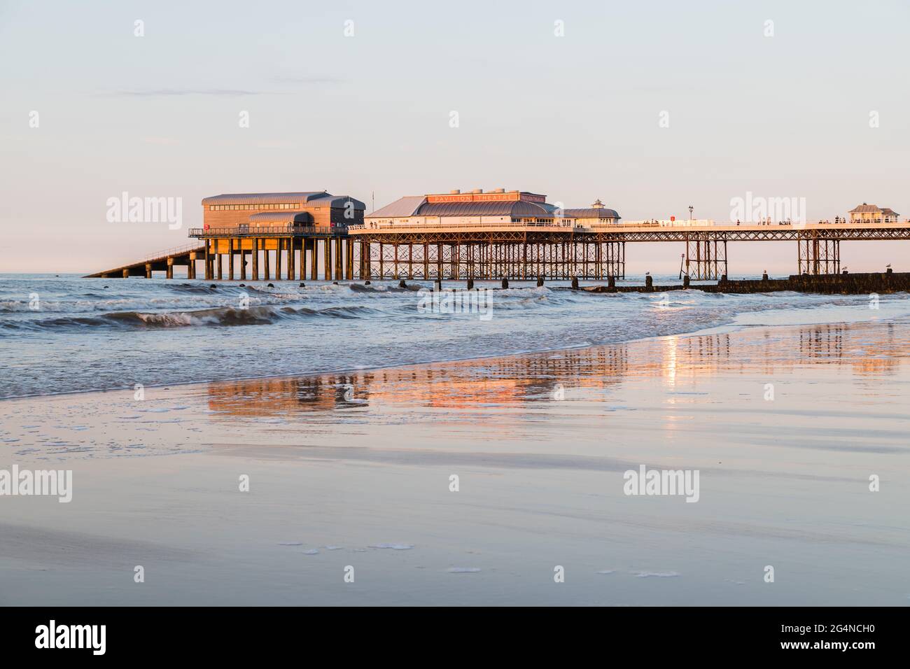 Cromer pier at sunset seen in June 2021 from the West beach with the sun lighting up the sandy beach. Stock Photo
