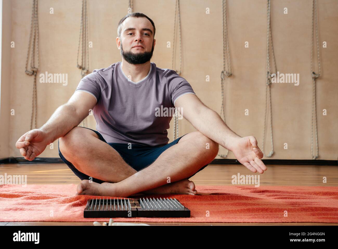 Man sitting in lotus pose with sadhu board in yoga studio meditating ...