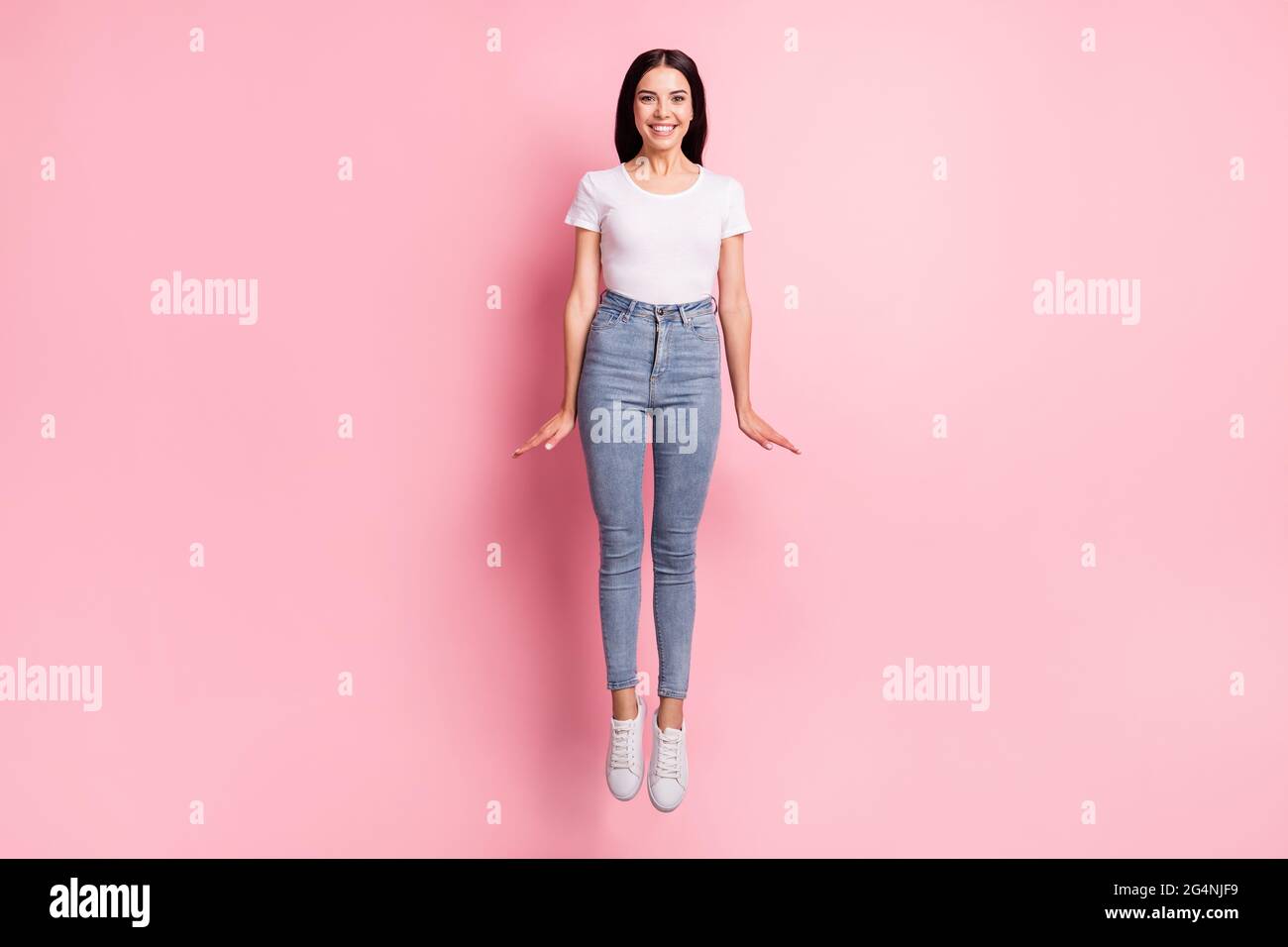 Full size photo of optimistic brunette lady jump wear white t-shirt jeans  sneakers isolated on pastel pink color background Stock Photo - Alamy